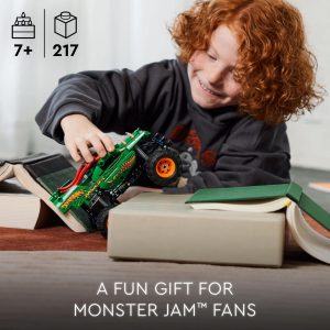 Young boy with red hair excitedly plays with a green monster truck toy indoors.
