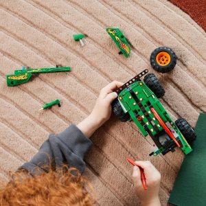 Child with red hair builds a colorful toy vehicle using vibrant building blocks on a rug.