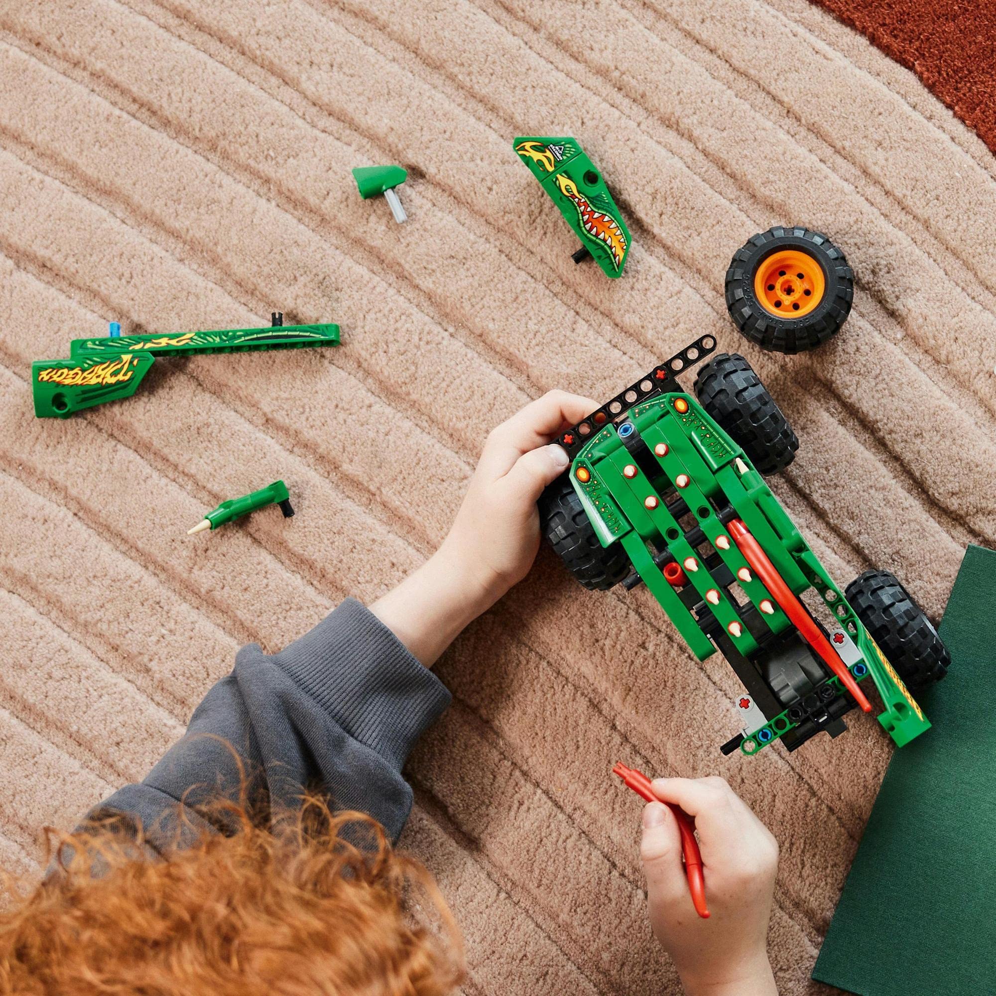 Child with red hair builds a colorful toy vehicle using vibrant building blocks on a rug.