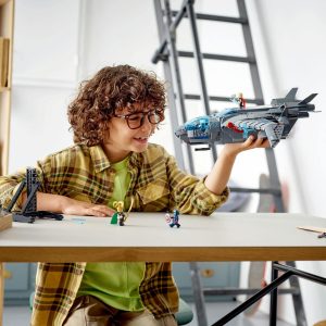 Young boy with glasses joyfully builds a toy aircraft while immersed in imaginative play.