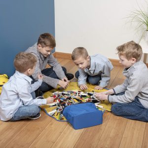 Boys in grey shirts joyfully playing with colorful blocks on a cozy yellow blanket.