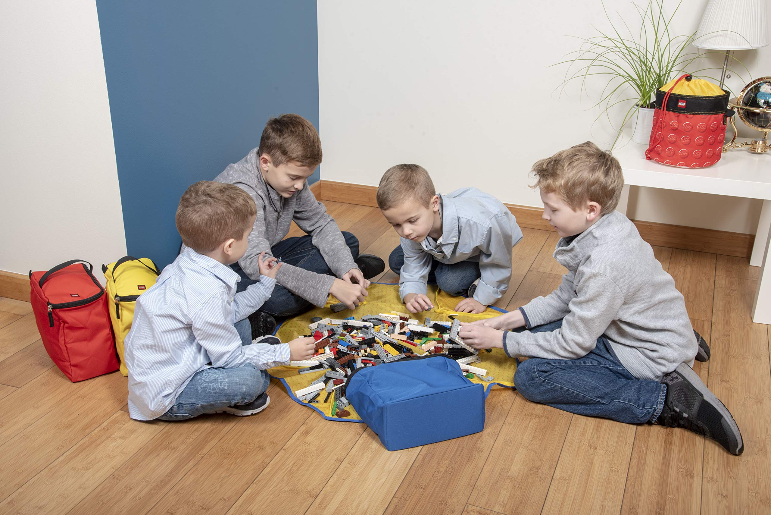 Boys in grey shirts joyfully playing with colorful blocks on a cozy yellow blanket.