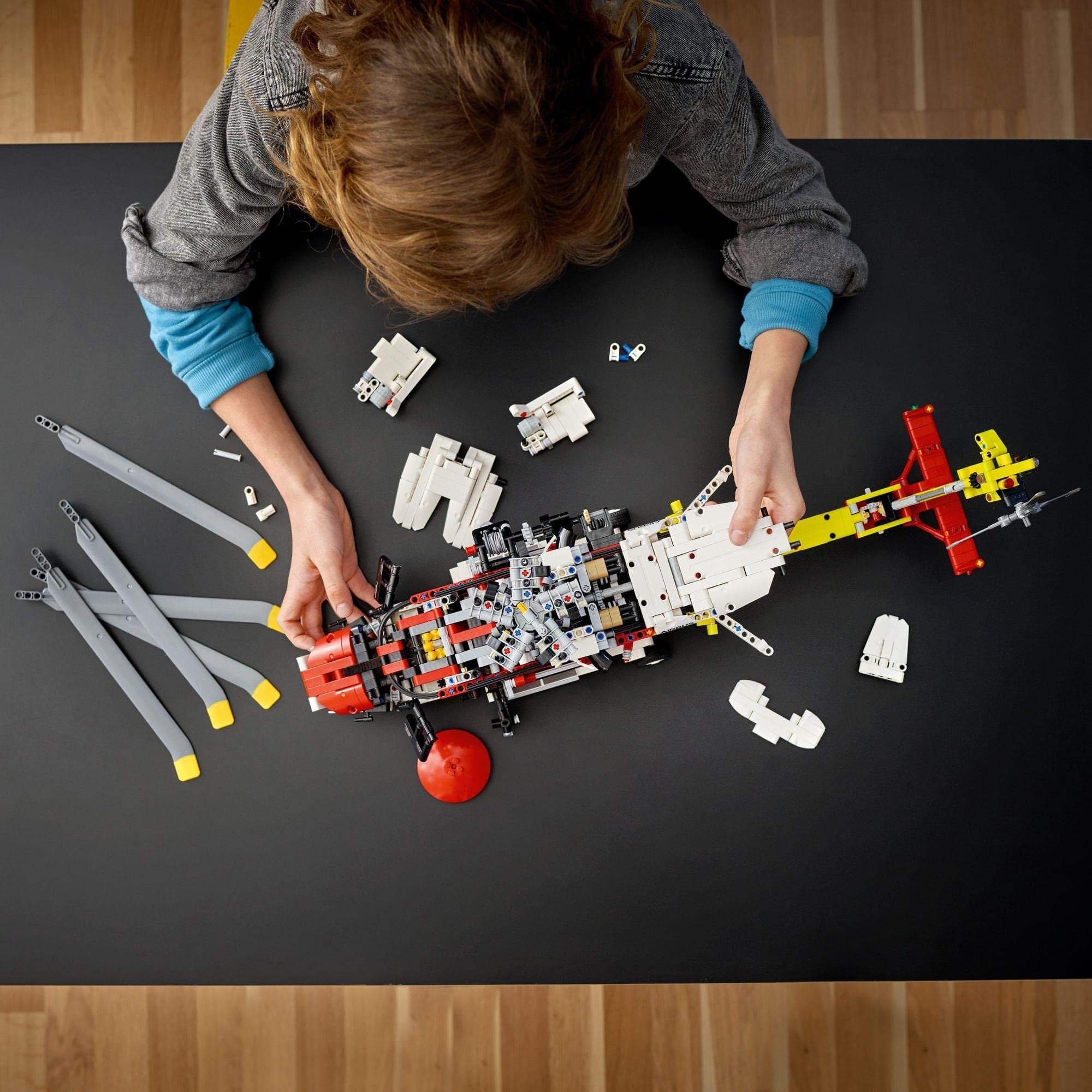 Child focused on building a colorful LEGO submarine amidst scattered bricks on a dark table.