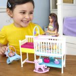 Joyful girl in yellow shirt playing with colorful dollhouse and doll at wooden table.