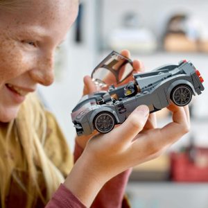 Young girl joyfully admires her detailed gray LEGO sports car in a creative play space.