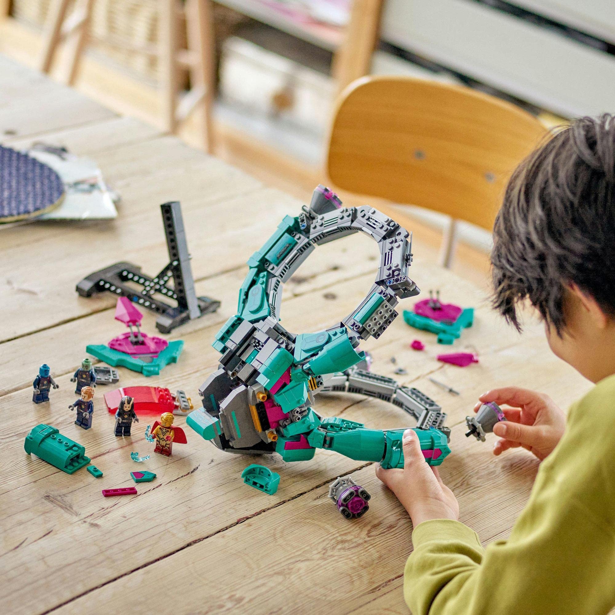 Child in yellow sweatshirt builds a colorful, imaginative structure with blocks on a wooden table.