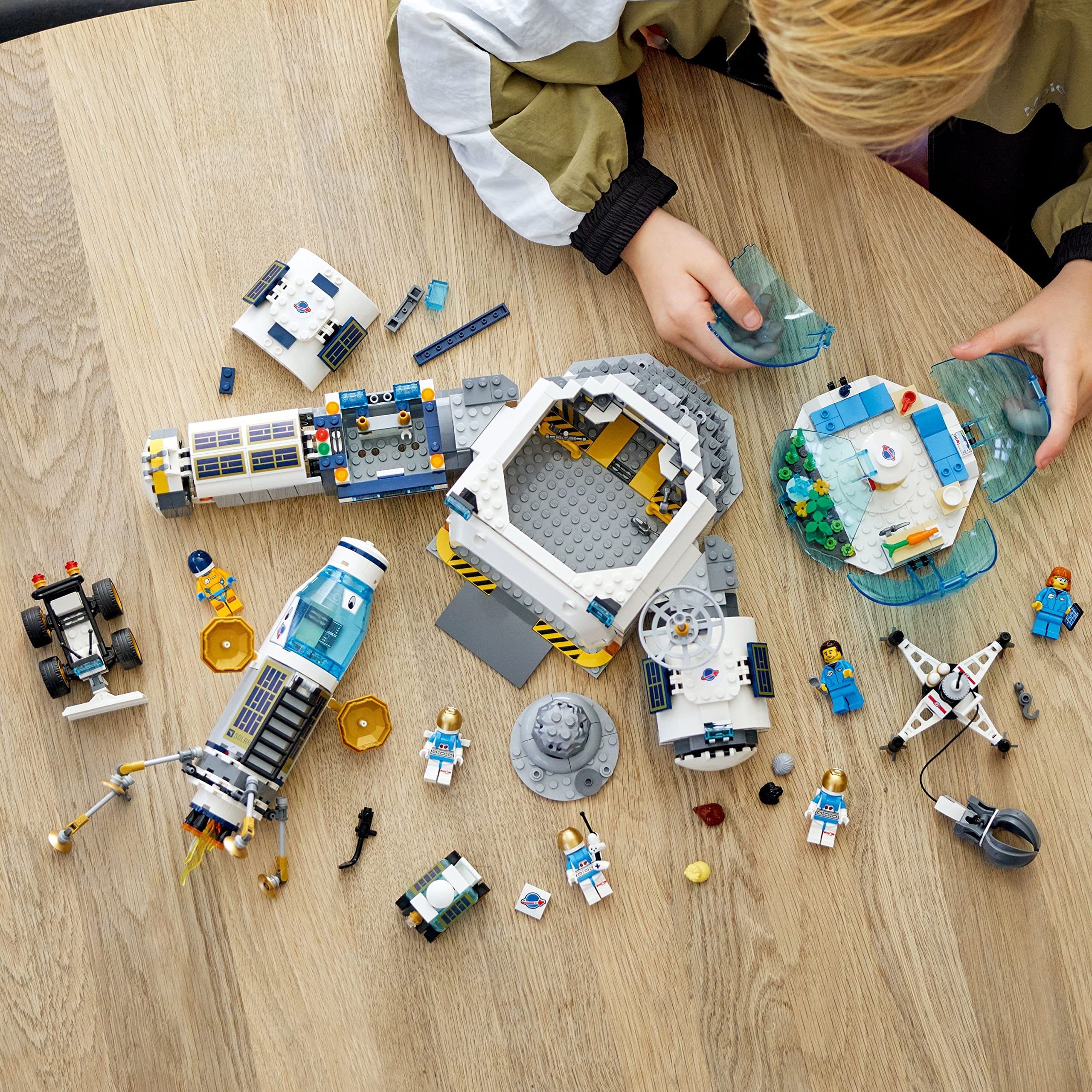 Child assembling a colorful Lego space playset on a wooden table, showcasing imaginative creativity.