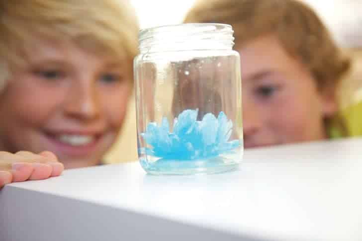 Boys fascinated by a vibrant blue science experiment in a jar, enjoying discovery together.