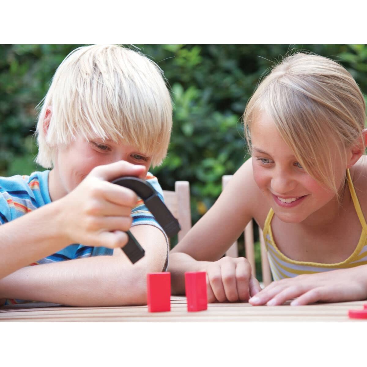 Children play with magnets at a wooden table in a bright outdoor setting.