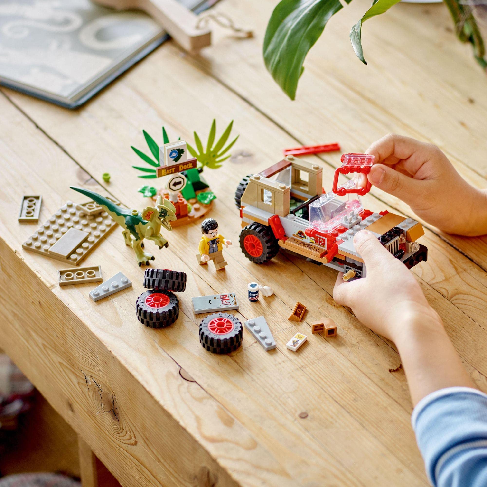 Child builds a vibrant LEGO off-road vehicle with mini adventurer on a wooden table.