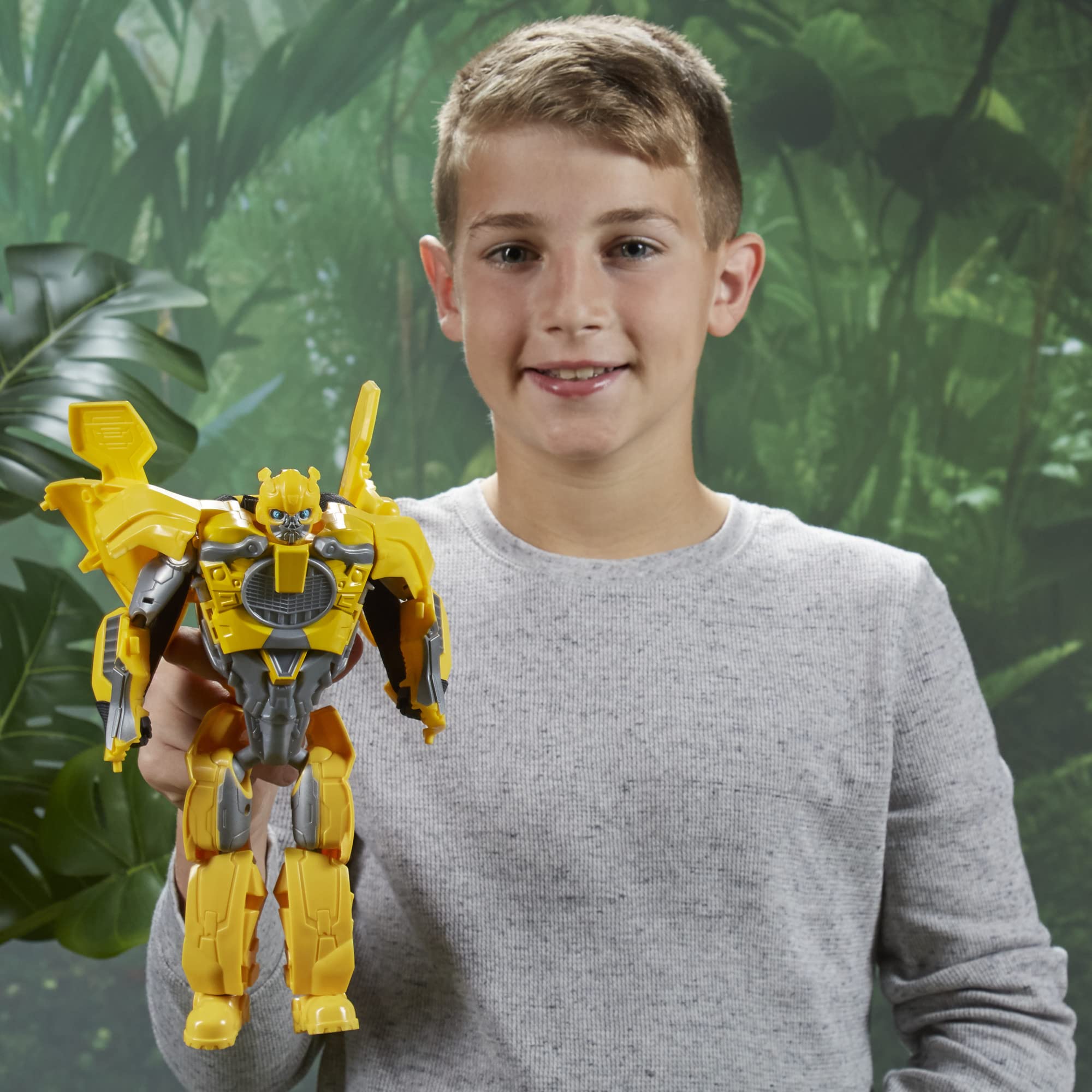 Joyful boy with Bumblebee Transformer toy in a lush, green outdoor setting.