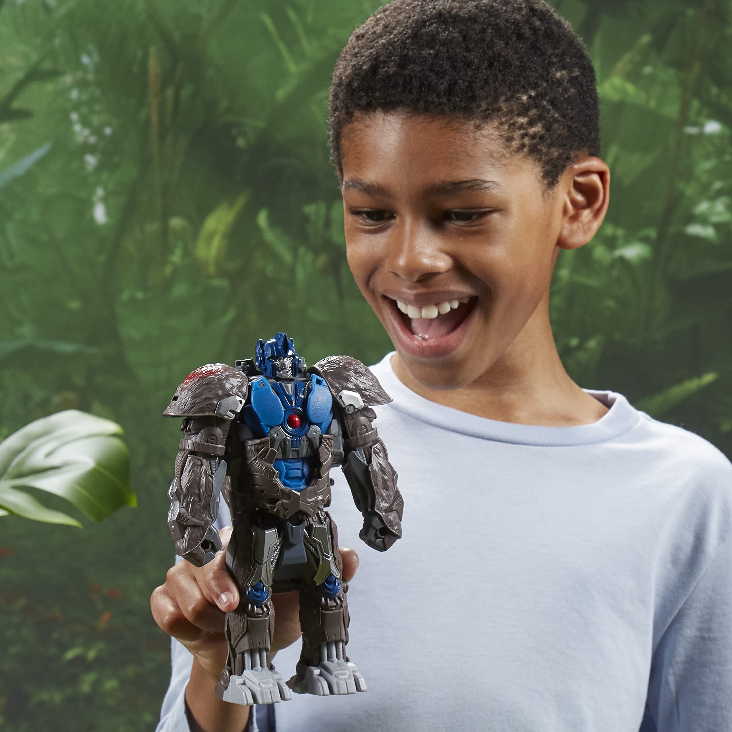 Happy boy joyfully playing with a blue robot action figure in a vibrant outdoor setting.