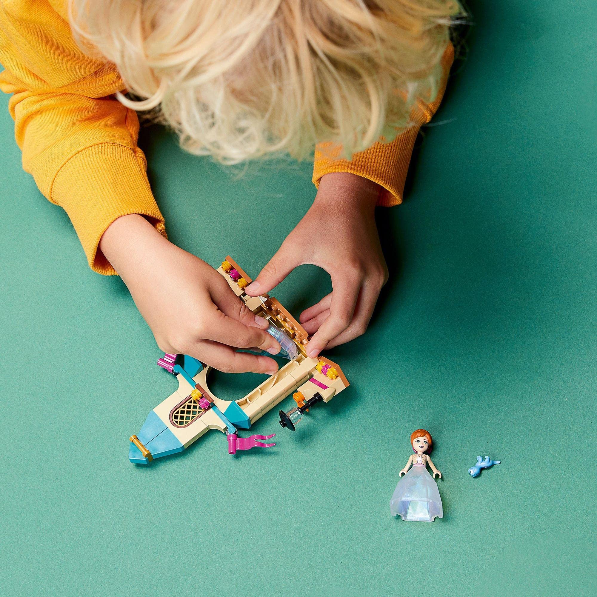 Child in yellow sweater joyfully builds colorful castle, sparking imagination during playtime.