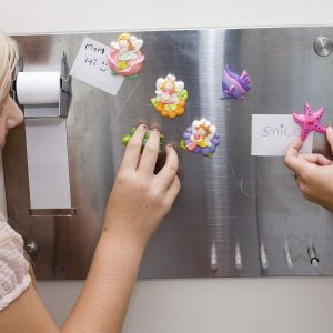 Joyful girls decorating a magnetic board with colorful magnets, showcasing creativity and friendship.