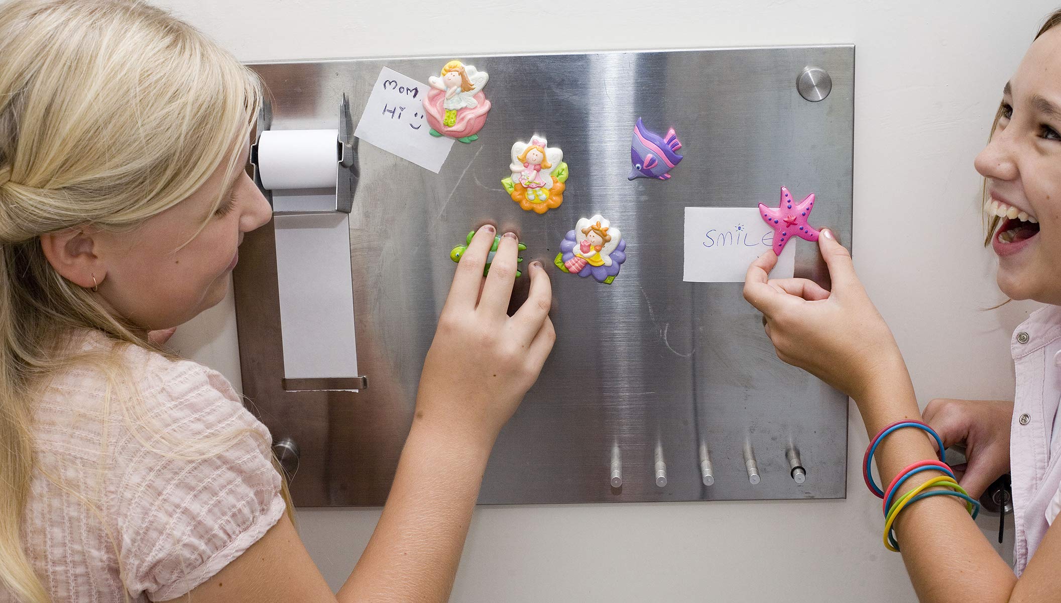 Joyful girls decorating a magnetic board with colorful magnets, showcasing creativity and friendship.
