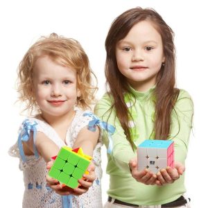 Two smiling girls holding colorful Rubiks Cubes against a bright white background.