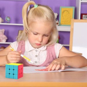 Young girl drawing intently, colorful Rubiks Cube nearby in a cozy creative space.
