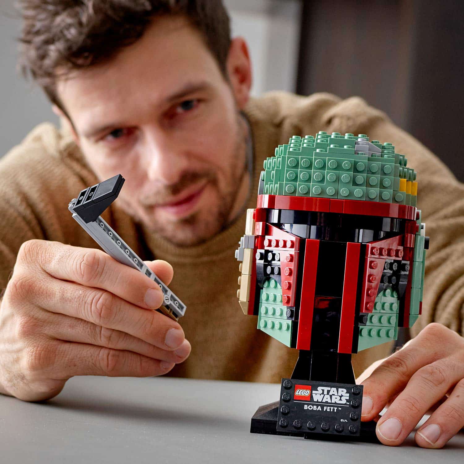 Man meticulously builds a LEGO Boba Fett helmet in a cozy, well-lit space.