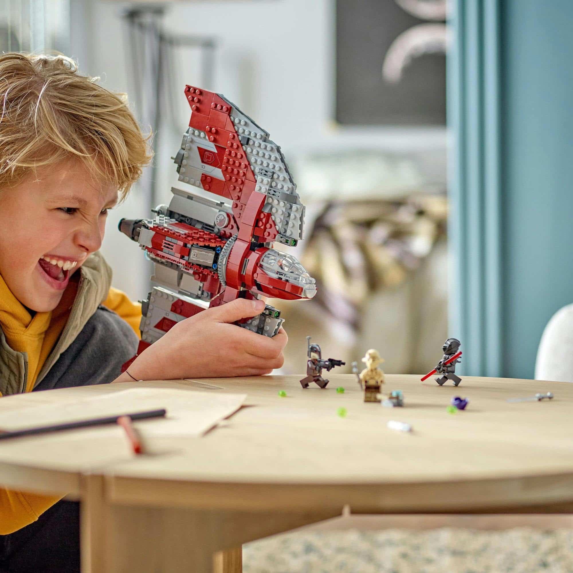 Joyful boy playing with colorful LEGO spaceship and action figures in a cozy, bright room.