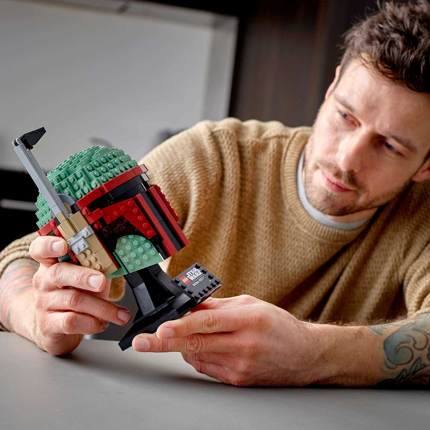Man admires a detailed Lego Star Wars bounty hunter helmet in a modern workspace.