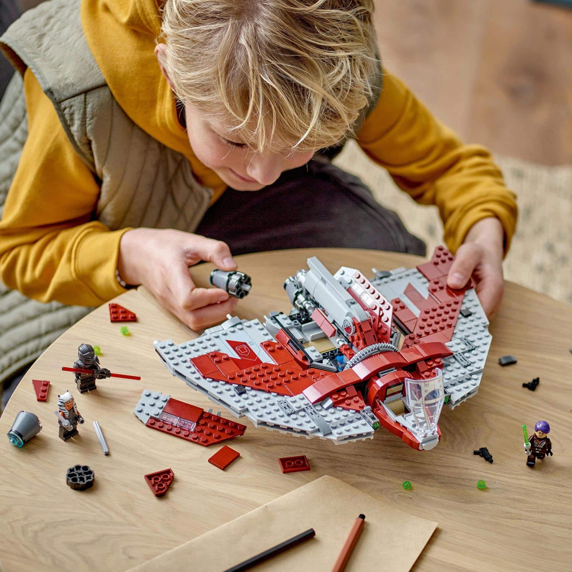 Young boy builds a red and gray LEGO spaceship, showcasing creativity and problem-solving skills.