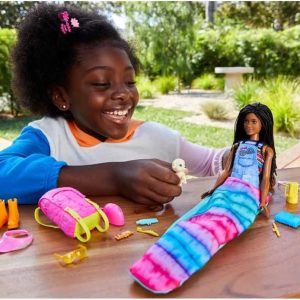 Girl happily styles colorful mermaid doll outdoors, surrounded by greenery and playfulness.