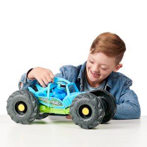 Joyful boy in denim jacket plays with vibrant blue monster truck, embodying childhood excitement.