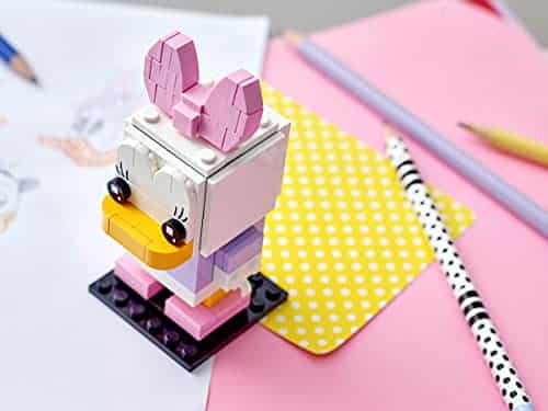 Colorful LEGO cartoon character with bunny ears in a creative workspace of drawings and supplies.