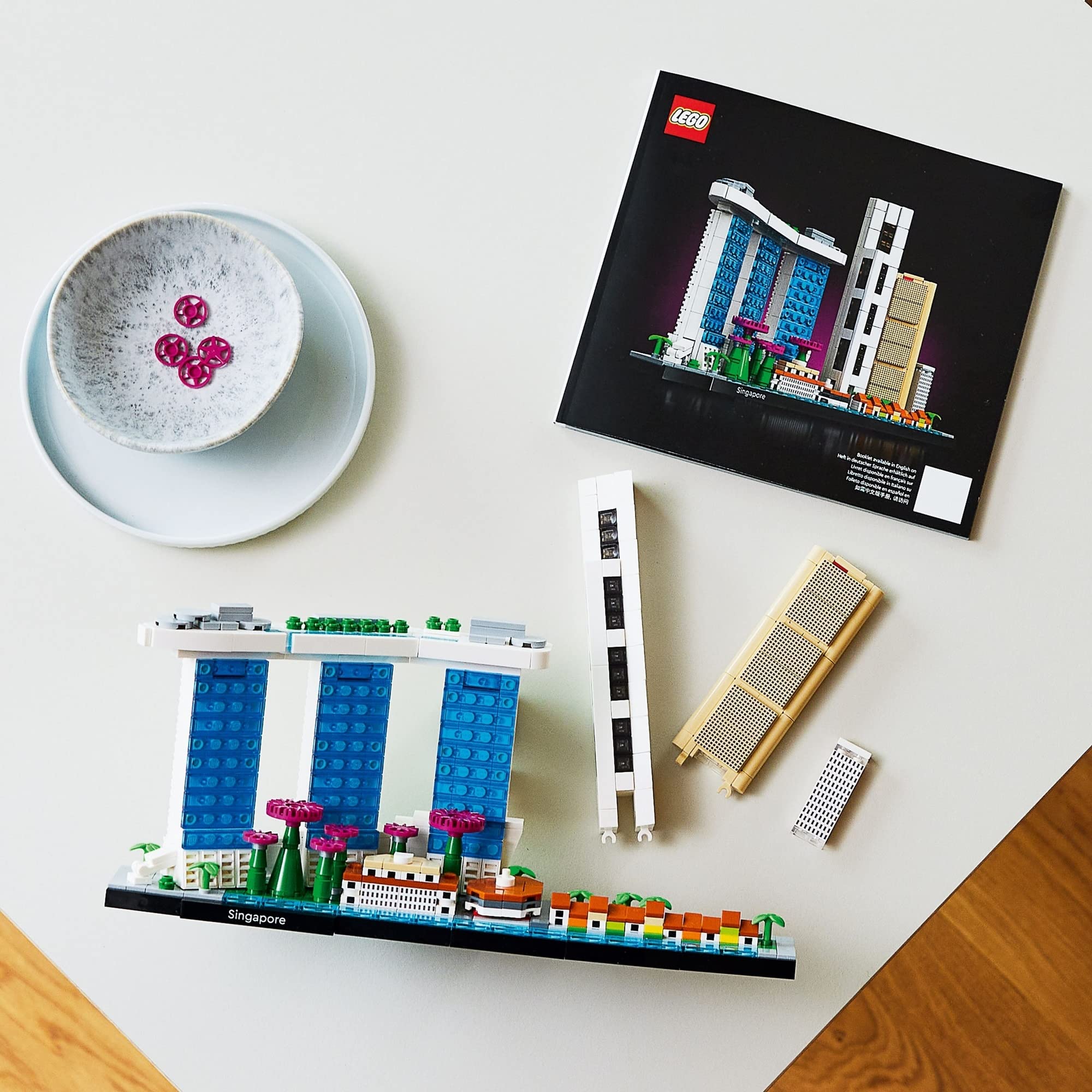LEGO architecture model under construction with vibrant pieces and whimsical bowl on warm wood surface.