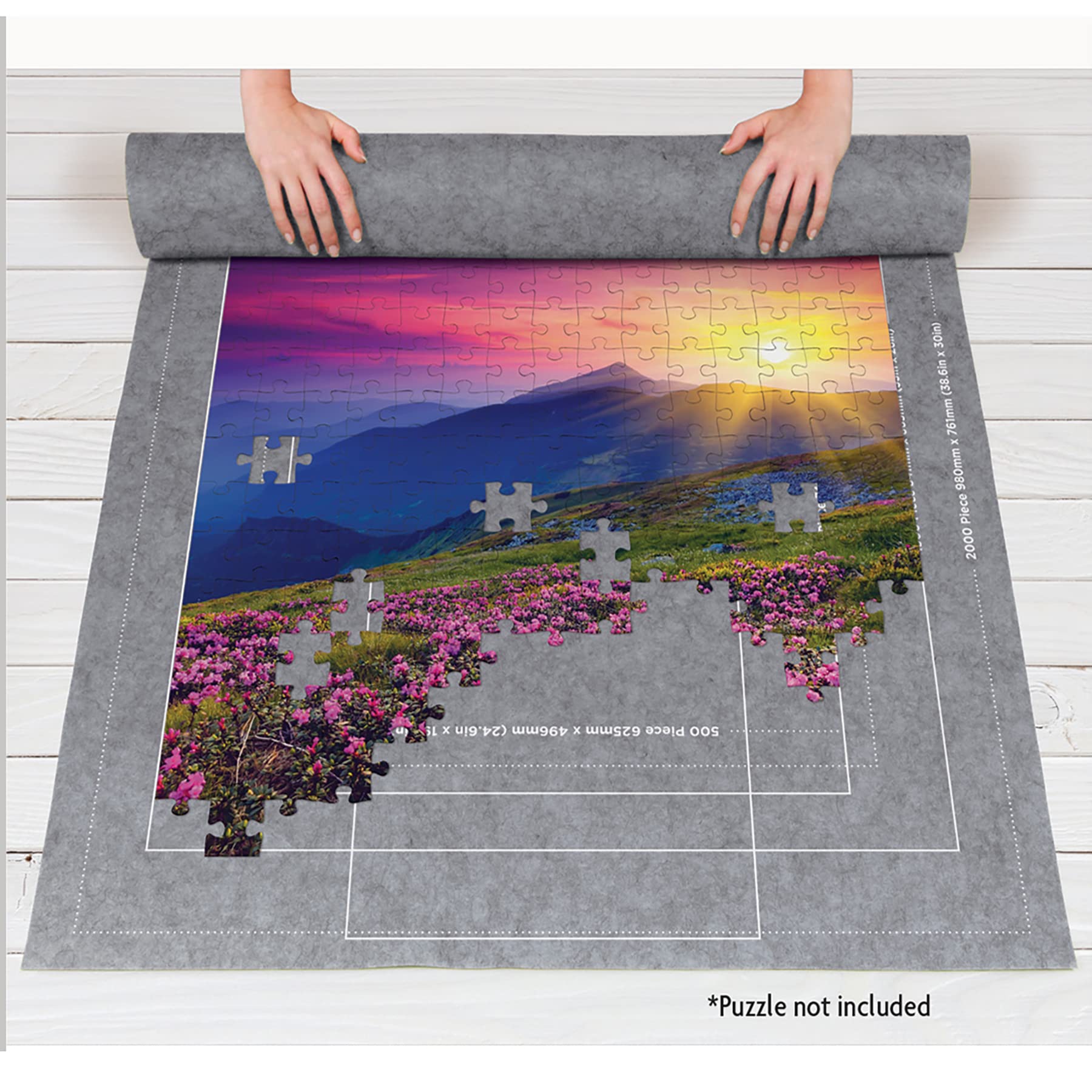 Hands assembling a scenic jigsaw puzzle on a textured rolling mat on wooden floor.