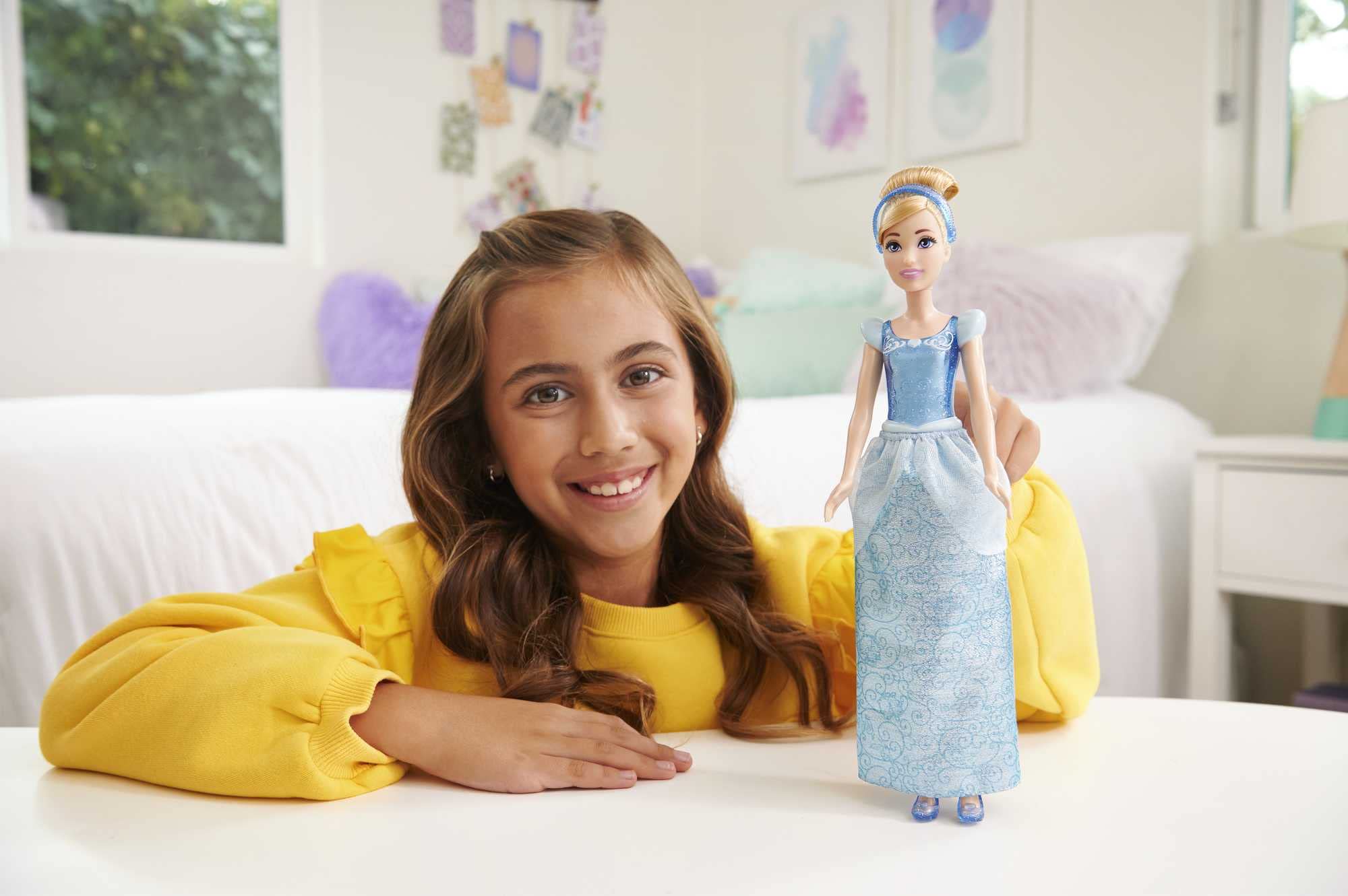 Joyful girl in yellow sweater plays with princess doll in cozy, pastel room.