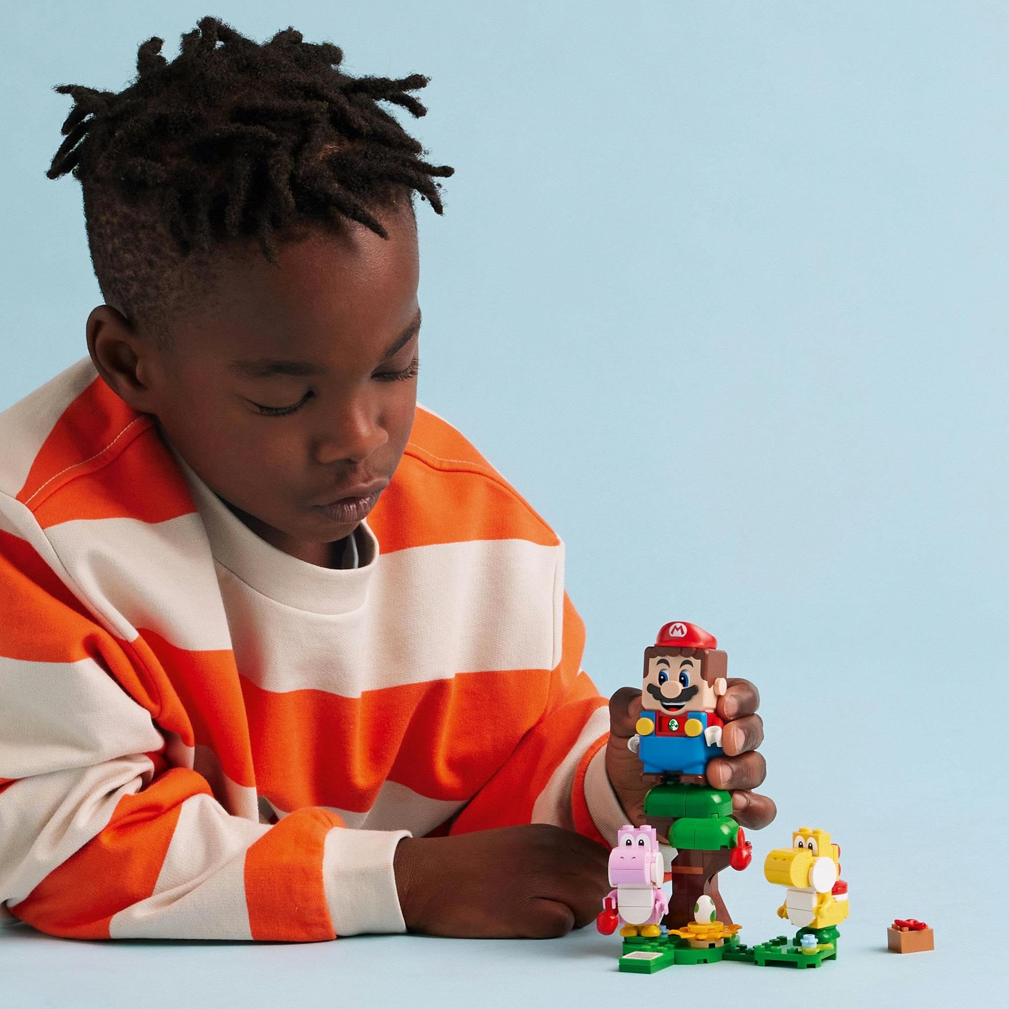 Young boy in striped sweater creatively playing with colorful toys against a light blue background.