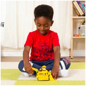 Cheerful boy plays with a yellow bulldozer on a cozy rug in a vibrant room.