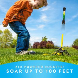 Excited boy launching kid-powered rocket outdoors on a sunny day surrounded by green nature.