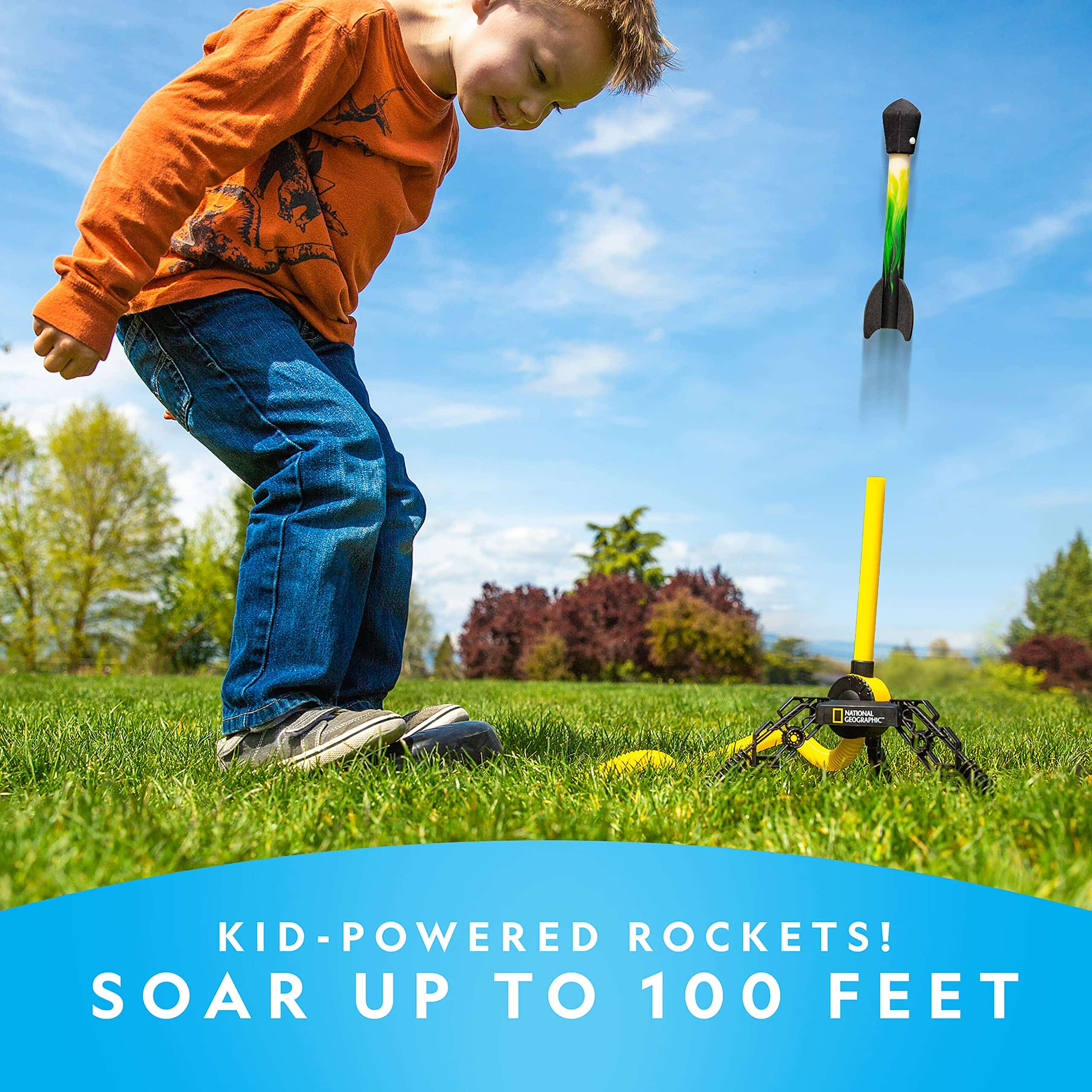 Excited boy launching kid-powered rocket outdoors on a sunny day surrounded by green nature.