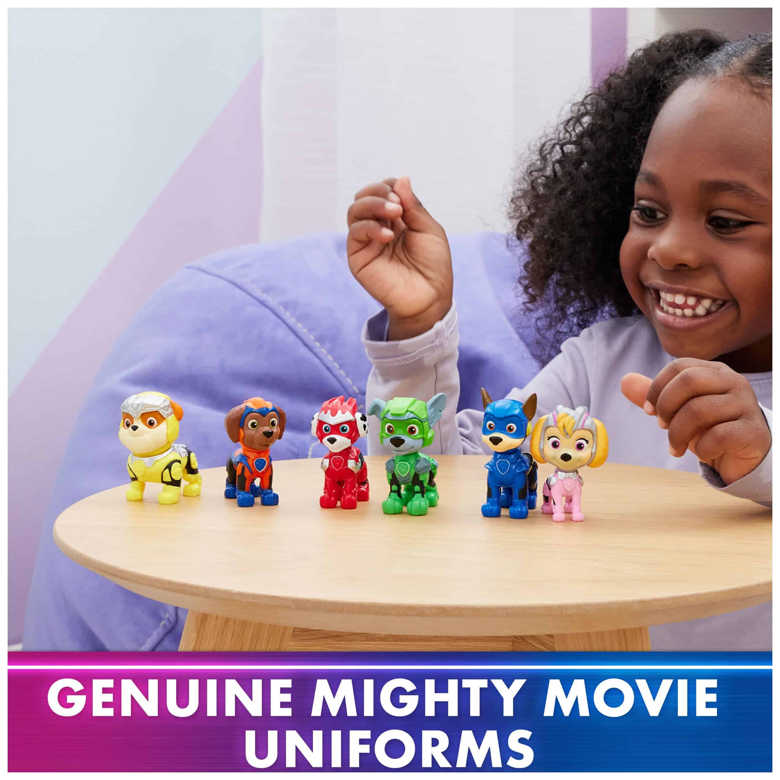 Young girl joyfully plays with colorful Mighty Movie toy figures at a wooden table.