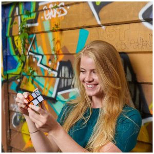 Joyful girl solving a Rubiks Cube against a colorful graffiti backdrop.