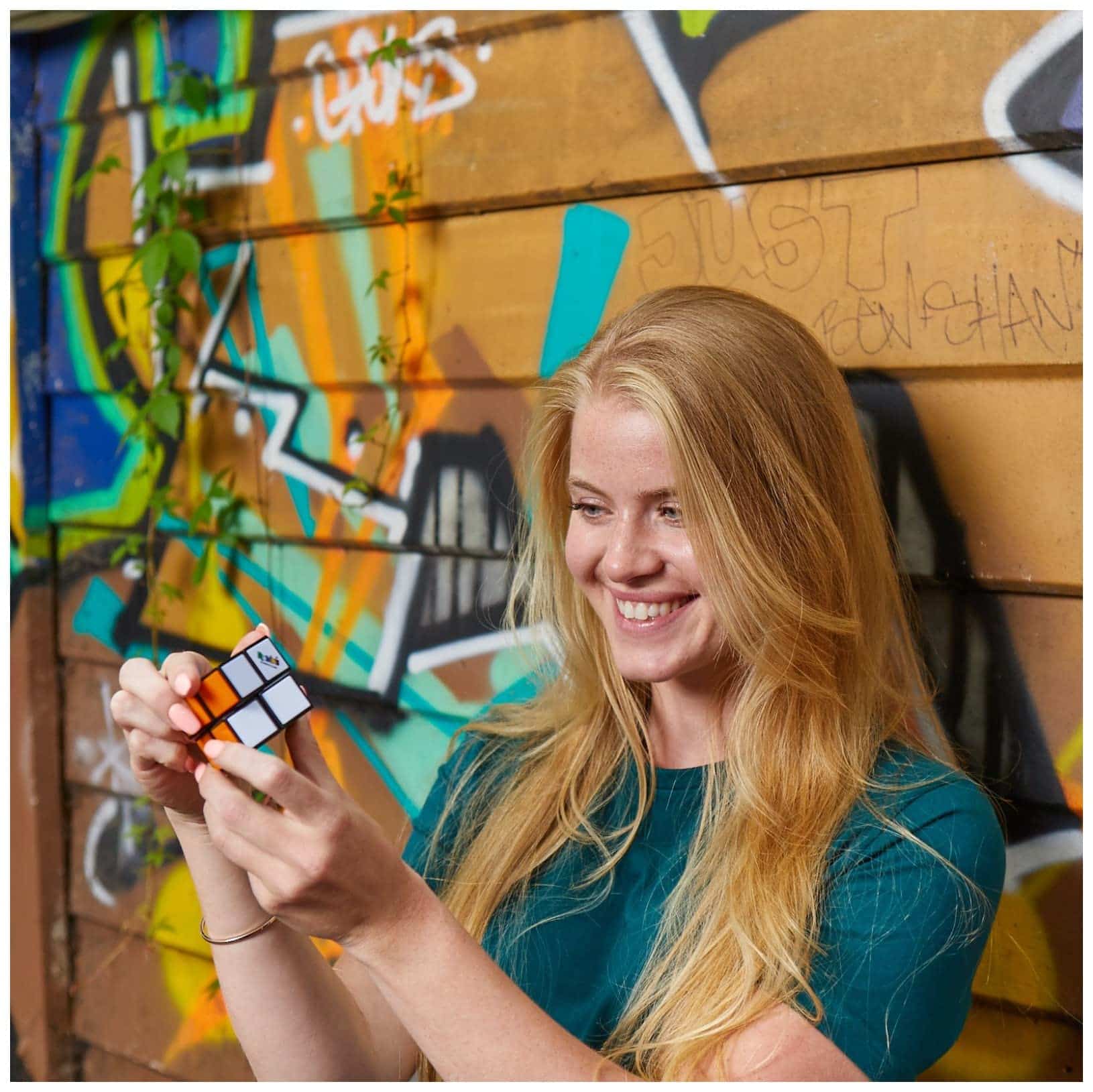 Joyful girl solving a Rubiks Cube against a colorful graffiti backdrop.