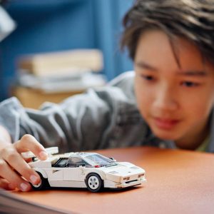 Young boy delightfully examines a white toy car in a cozy, book-filled room.