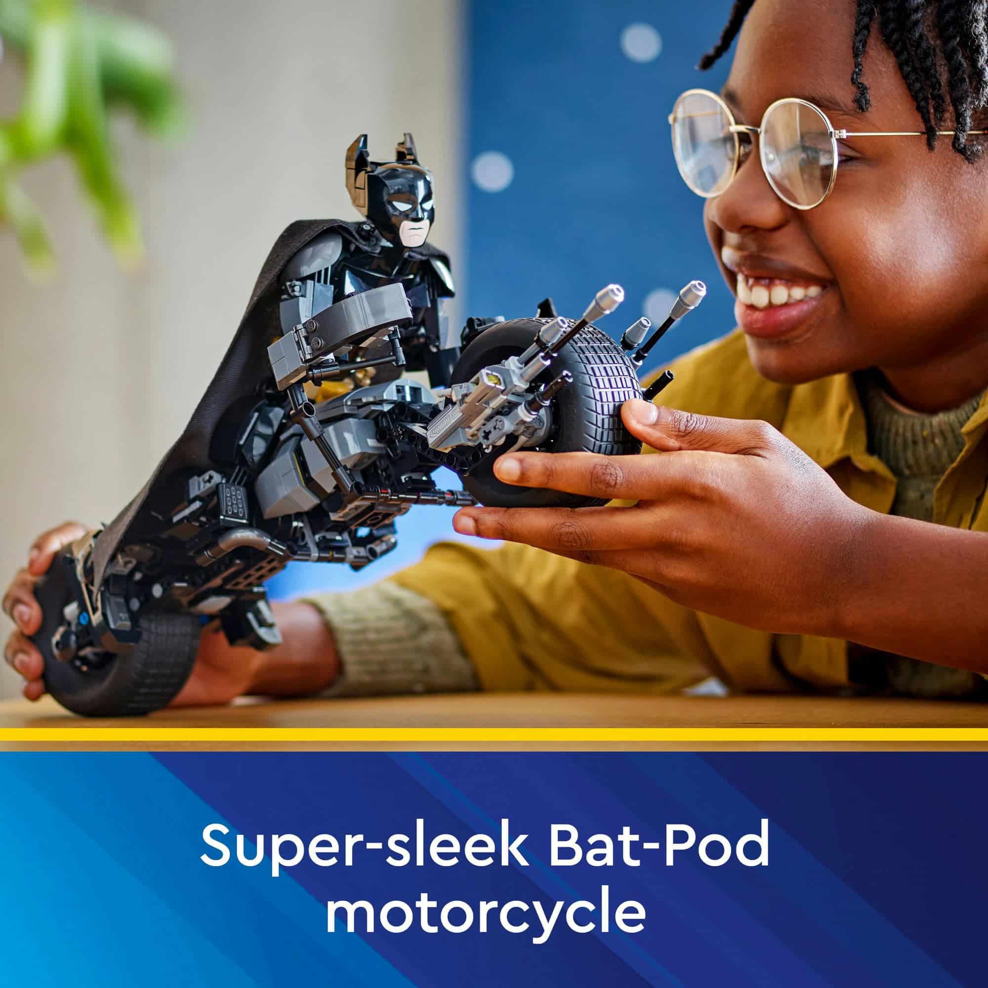 Joyful child in yellow shirt plays with detailed Bat-Pod motorcycle toy from Batman franchise.