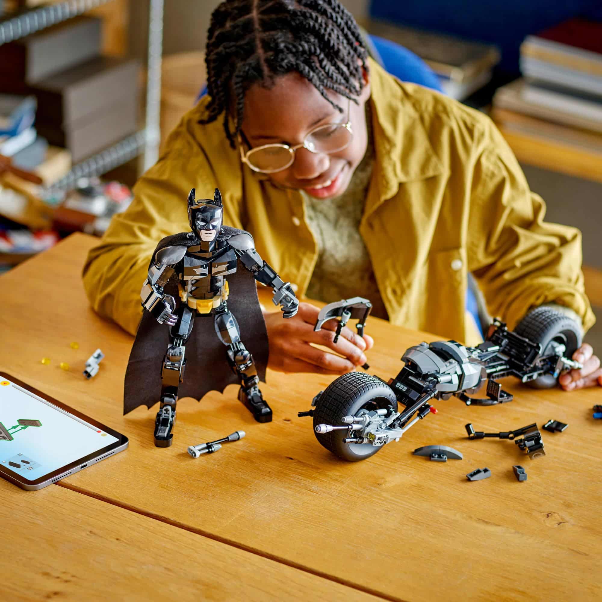 Child builds a Batman motorbike model using a tablet for guidance in a cozy setting.