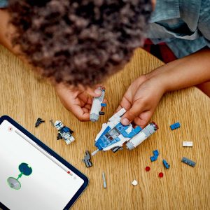 Child constructs a colorful spacecraft with digital guidance on a wooden table.
