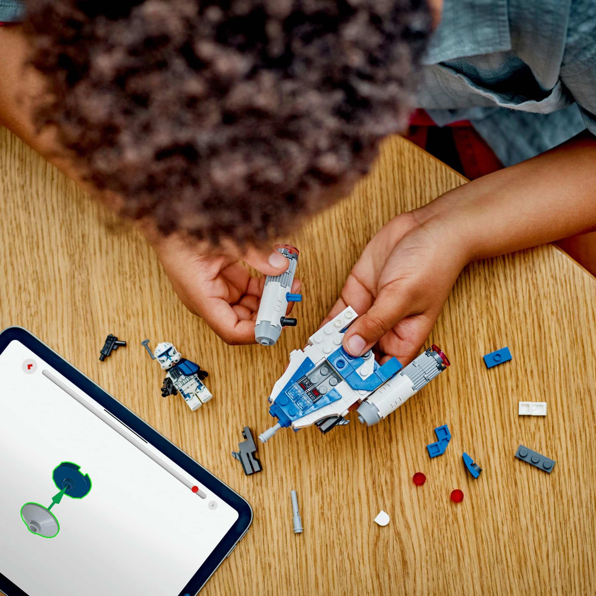 Child constructs a colorful spacecraft with digital guidance on a wooden table.