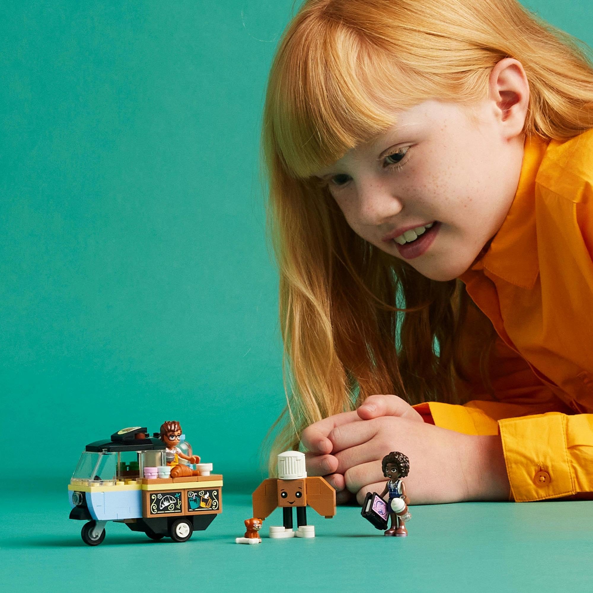 Child with red hair happily plays with a colorful toy food truck and figures.