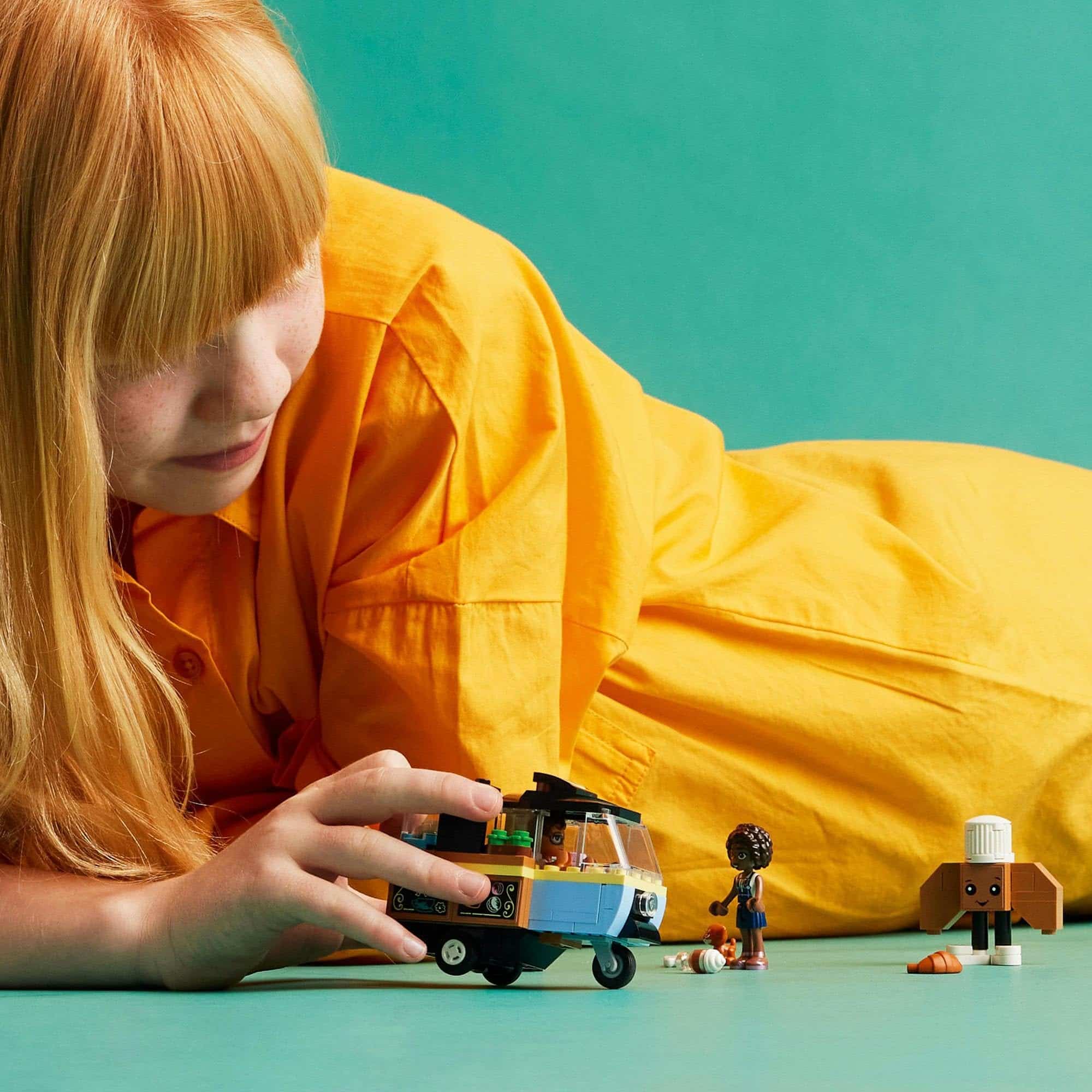 Young girl with golden hair joyfully plays with colorful toys on a turquoise surface.