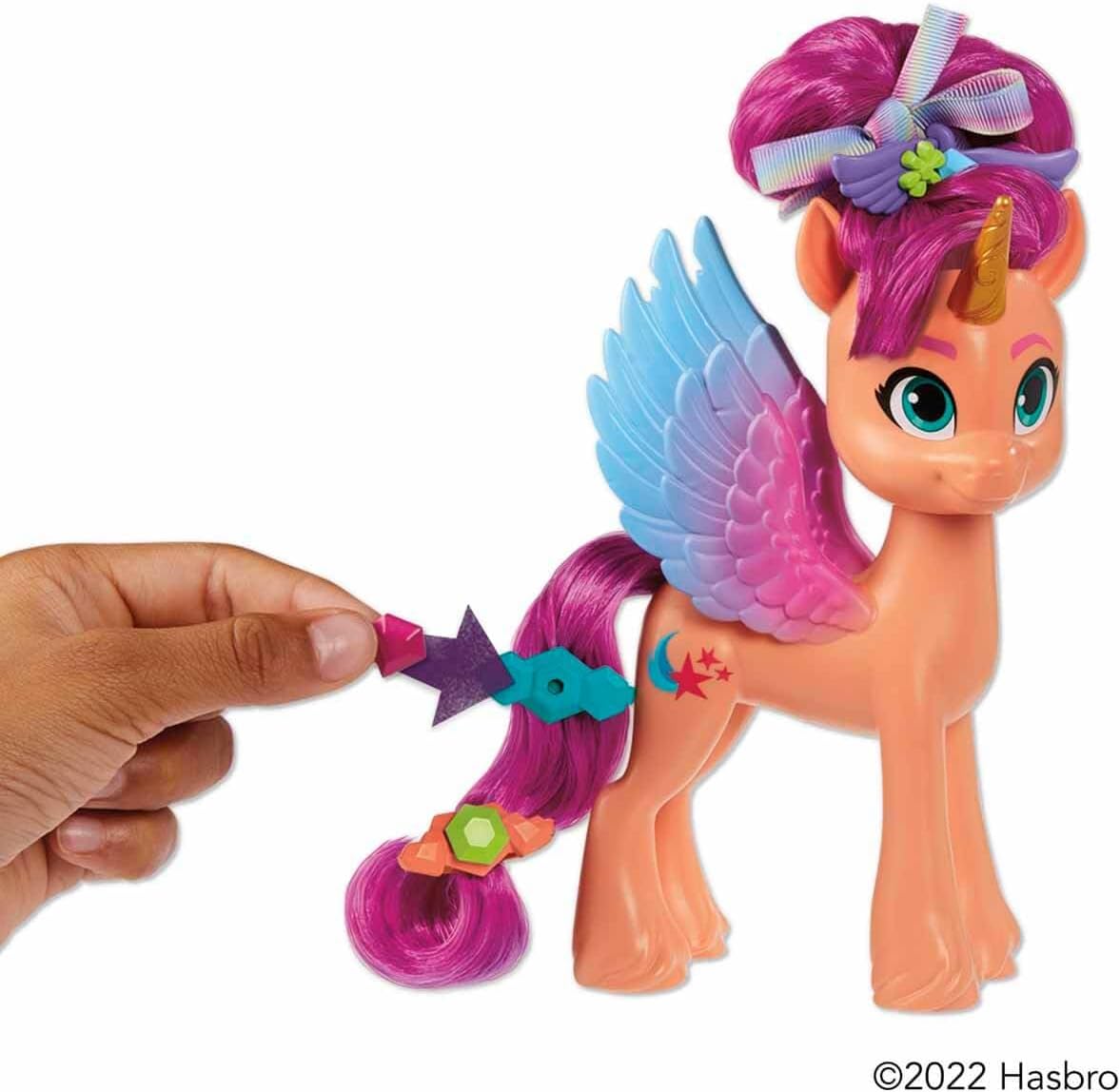 Colorful coral-pink pony toy with blue wings, unicorn horn, and customizable hair accessories for imaginative play.