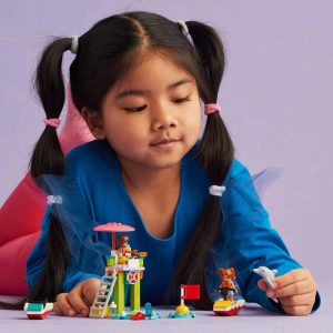 Young girl with pigtails joyfully builds a colorful toy world with lifeguard tower and boats.