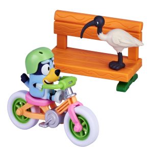 Playful blue dog rides bicycle in vibrant park with ibis bird and colorful bench.