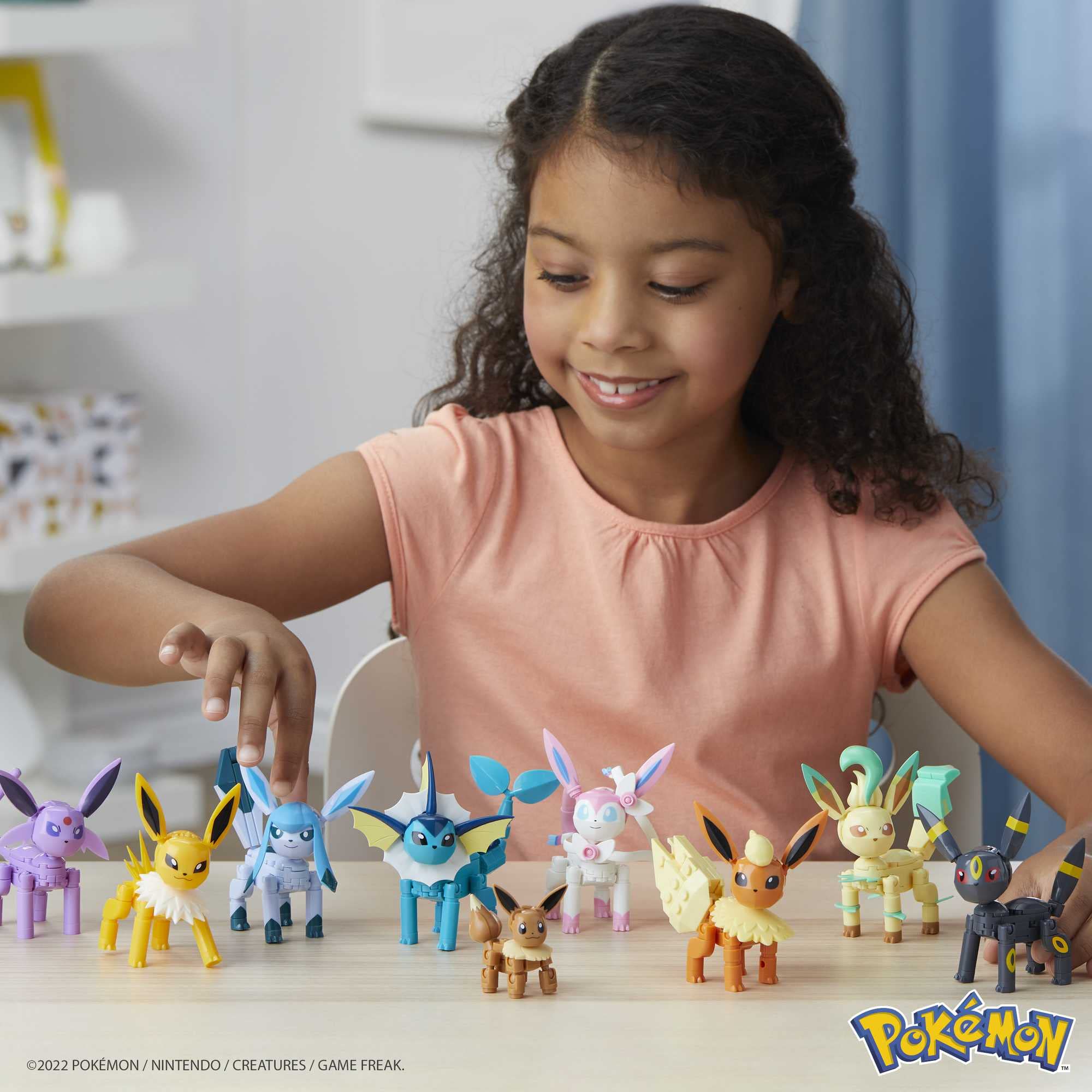 Young girl joyfully plays with colorful Eevee evolution figures, sparking creativity and imagination.