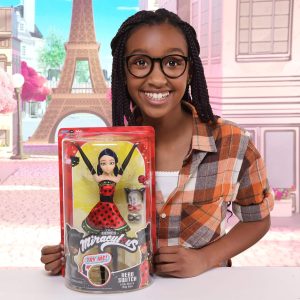 Joyful girl holds Miraculous Ladybug doll with Eiffel Tower backdrop, celebrating childhood imagination.